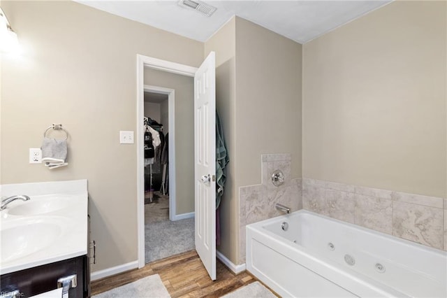 full bath featuring wood finished floors, a jetted tub, double vanity, and baseboards
