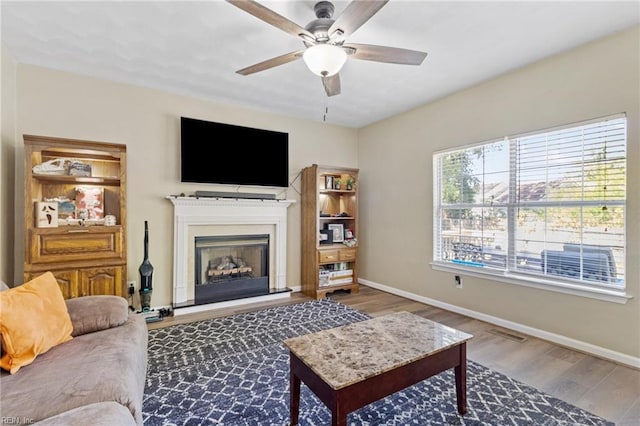 living area with wood finished floors, a ceiling fan, baseboards, and a fireplace with raised hearth