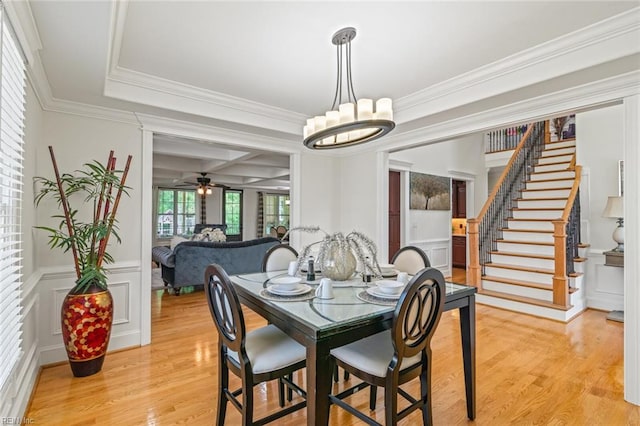 dining space featuring light wood-style flooring, crown molding, a decorative wall, stairway, and a chandelier