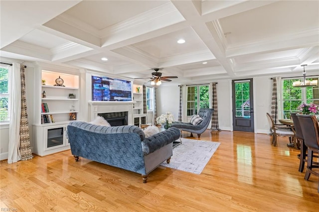 living room featuring healthy amount of natural light, light wood finished floors, a fireplace, a ceiling fan, and crown molding