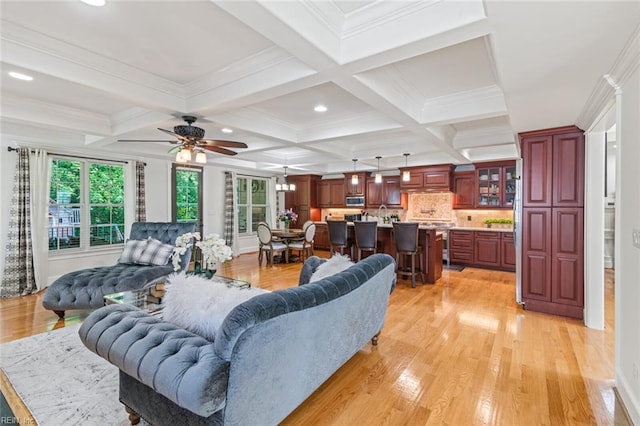 living room with plenty of natural light, light wood-type flooring, beam ceiling, ceiling fan, and coffered ceiling