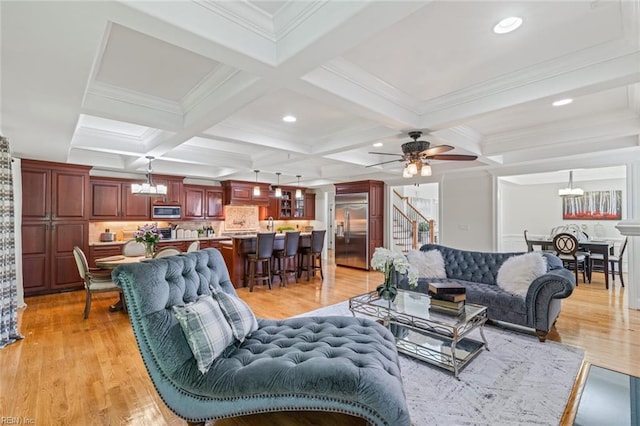 living room featuring a chandelier, beamed ceiling, coffered ceiling, ceiling fan, and light wood-style flooring