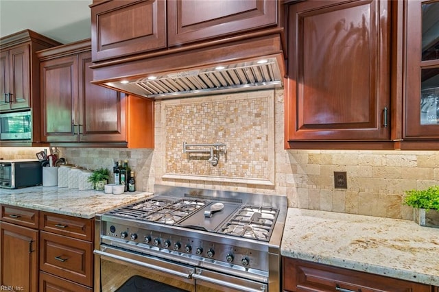 kitchen with stainless steel appliances, custom exhaust hood, decorative backsplash, light stone countertops, and glass insert cabinets
