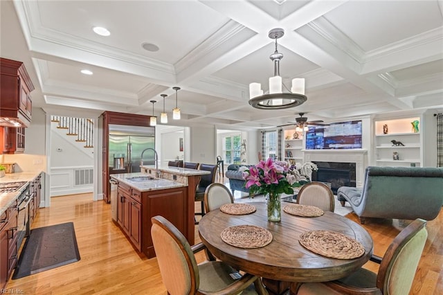 dining area with light wood finished floors, ceiling fan, a premium fireplace, coffered ceiling, and beamed ceiling
