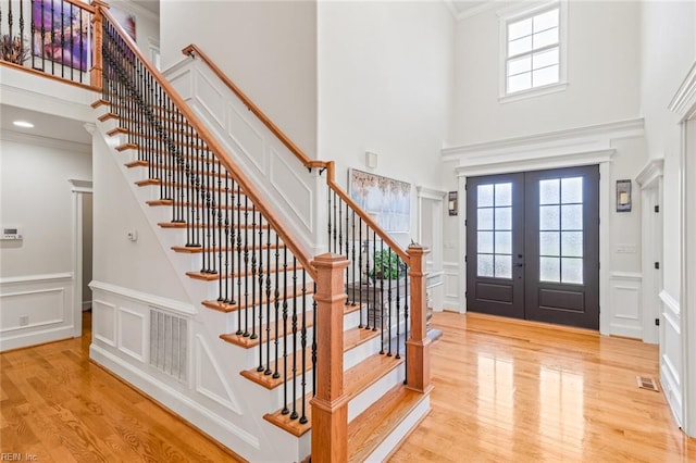 entrance foyer with a decorative wall, healthy amount of natural light, a towering ceiling, light wood-style floors, and stairway
