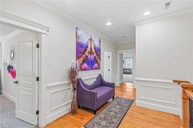 hallway featuring a decorative wall, wood finished floors, crown molding, a wainscoted wall, and recessed lighting