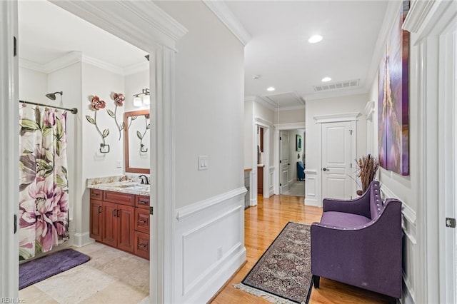 hall with wainscoting, crown molding, recessed lighting, and a sink
