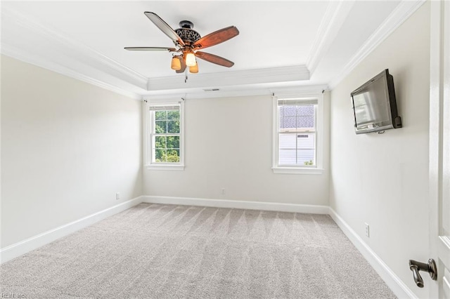 empty room featuring ornamental molding, a raised ceiling, baseboards, a ceiling fan, and carpet flooring