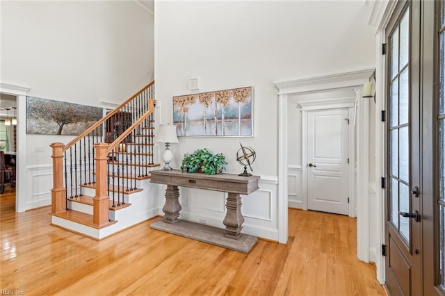 entrance foyer with light wood-type flooring, a high ceiling, stairs, a decorative wall, and a wainscoted wall