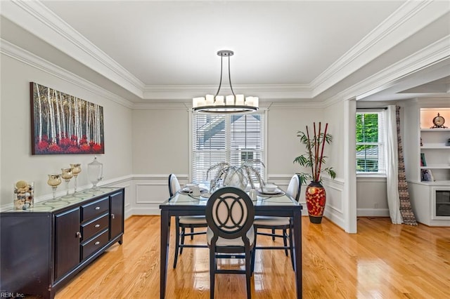 dining space with a chandelier, light wood finished floors, ornamental molding, a tray ceiling, and a wainscoted wall