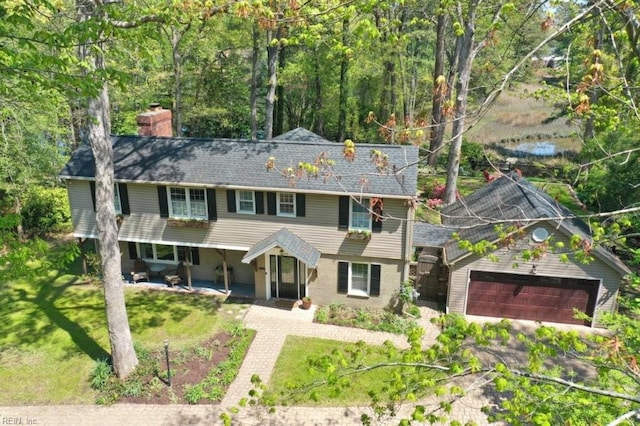 colonial inspired home with a chimney, asphalt driveway, an attached garage, and a front yard
