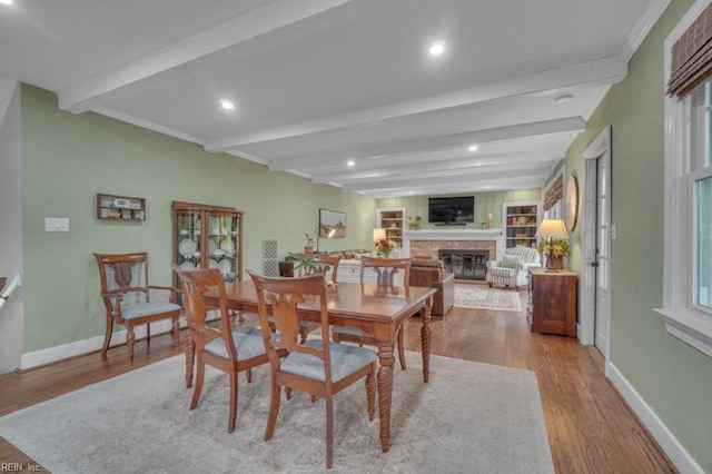 dining area featuring wood finished floors, baseboards, beamed ceiling, a brick fireplace, and recessed lighting