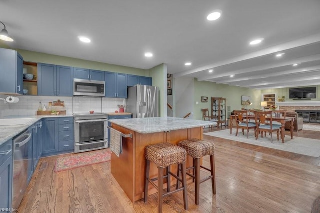 kitchen with appliances with stainless steel finishes, blue cabinetry, a kitchen bar, a center island, and backsplash