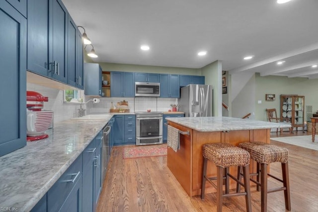 kitchen featuring stainless steel appliances, a sink, blue cabinets, light wood-style flooring, and recessed lighting