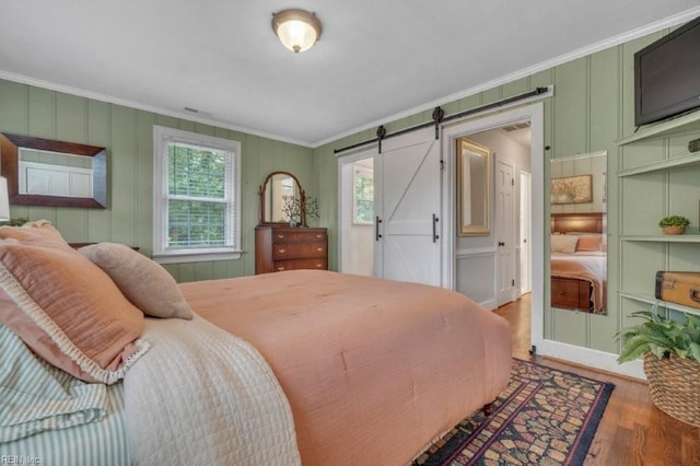 bedroom featuring crown molding, multiple windows, wood finished floors, a barn door, and a decorative wall