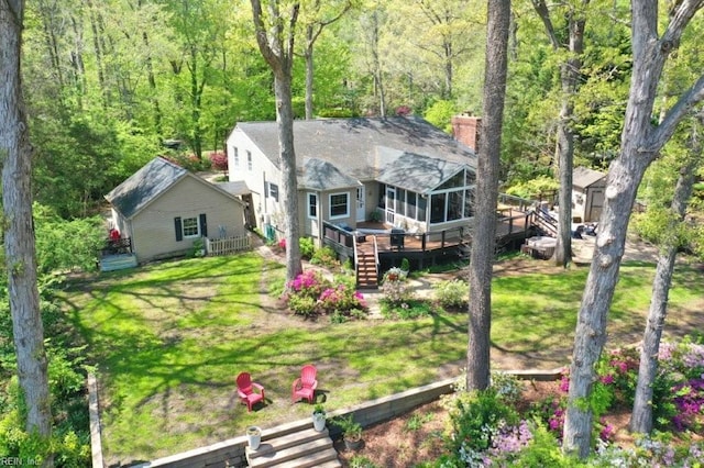 back of house featuring a deck, a chimney, stairs, a view of trees, and a sunroom