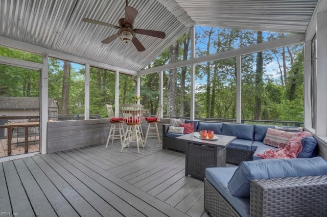 sunroom / solarium with an outdoor hangout area, a ceiling fan, vaulted ceiling, and view of wooded area
