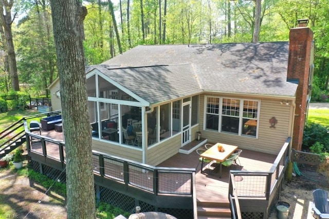 rear view of house with roof with shingles, a sunroom, a wooden deck, a chimney, and outdoor dining space