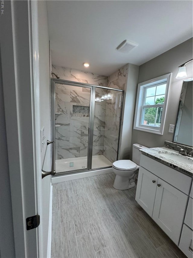 full bath with vanity, toilet, a marble finish shower, and wood finished floors