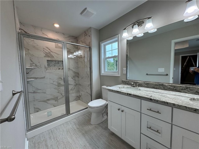 bathroom with a marble finish shower, toilet, double vanity, and wood finished floors
