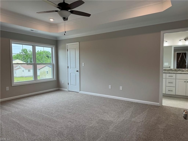 unfurnished bedroom featuring a raised ceiling, ornamental molding, light carpet, baseboards, and ensuite bath