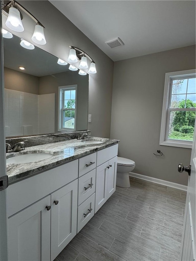 full bathroom with healthy amount of natural light, double vanity, toilet, and baseboards
