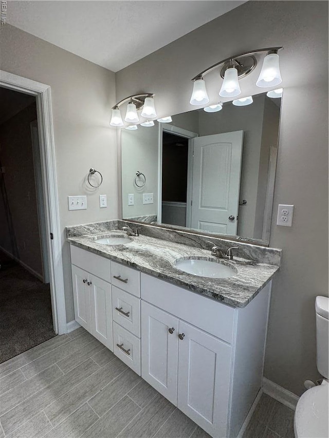 full bathroom featuring toilet, double vanity, and baseboards
