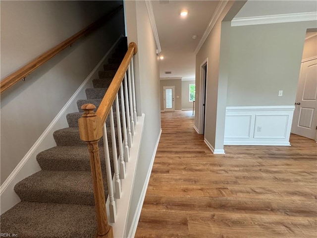 stairway with crown molding, wood finished floors, a wainscoted wall, and baseboards