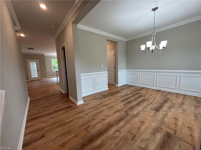 unfurnished dining area with crown molding, a chandelier, wood finished floors, wainscoting, and baseboards