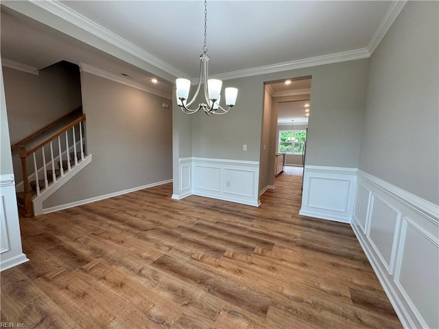 unfurnished dining area featuring a chandelier, wood finished floors, a wainscoted wall, crown molding, and stairs
