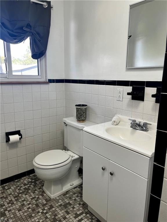 half bathroom with tile walls, toilet, wainscoting, vanity, and tile patterned floors