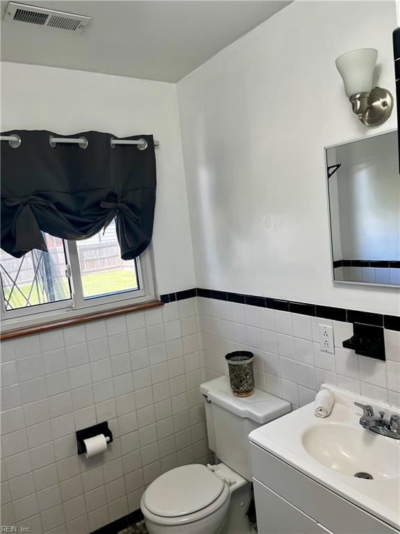 half bath with tile walls, toilet, wainscoting, and vanity