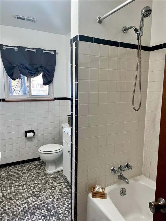 bathroom featuring toilet, tub / shower combination, and tile walls