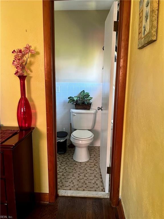bathroom with toilet, wainscoting, baseboards, and tile walls