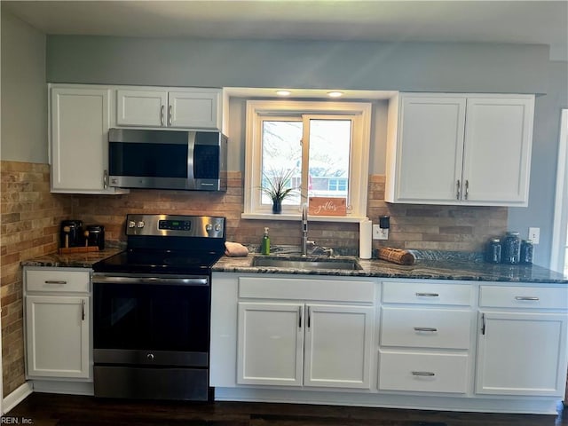 kitchen with stainless steel appliances, a sink, dark stone counters, and white cabinetry
