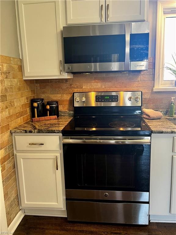 kitchen featuring stainless steel appliances, dark stone countertops, white cabinetry, and decorative backsplash