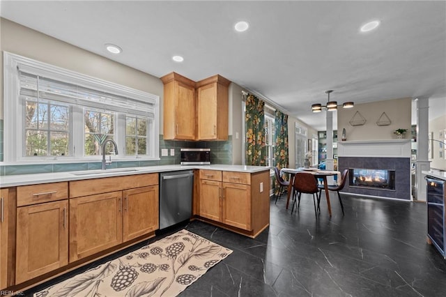 kitchen featuring stainless steel dishwasher, a sink, light countertops, a multi sided fireplace, and backsplash