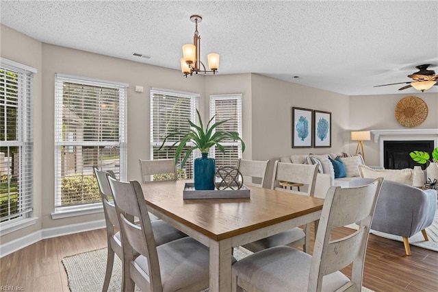 dining room featuring healthy amount of natural light, a chandelier, a textured ceiling, wood finished floors, and ceiling fan