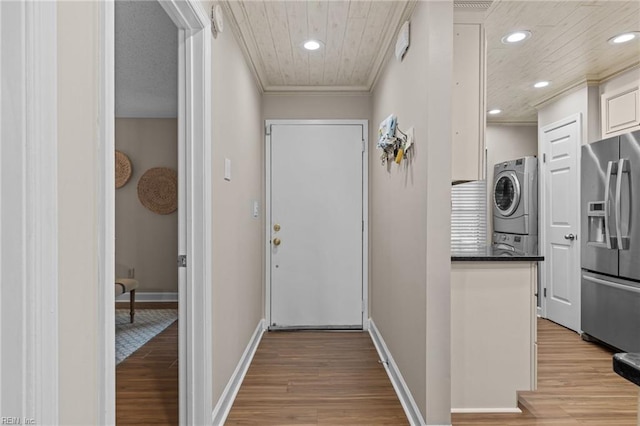 hallway featuring stacked washer / drying machine, light wood-type flooring, recessed lighting, crown molding, and baseboards