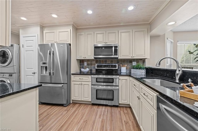 kitchen with stainless steel appliances, stacked washer and clothes dryer, a sink, crown molding, and light wood-style flooring