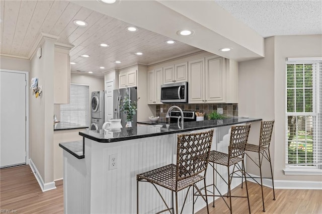 kitchen featuring appliances with stainless steel finishes, stacked washing machine and dryer, baseboards, light wood finished floors, and recessed lighting