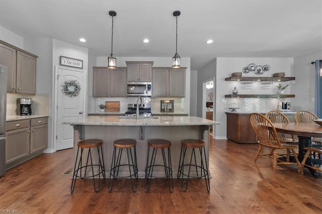 7935 Patriots Landing Pl, Quinton, VA 23141 - kitchen featuring stainless steel microwave, tasteful backsplash, a sink, dark wood-style floors, and a kitchen breakfast bar