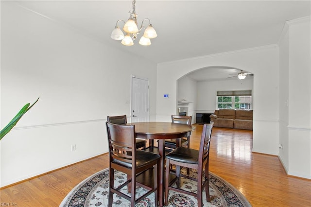 dining room featuring arched walkways, light wood-style flooring, a chandelier, ceiling fan, and crown molding