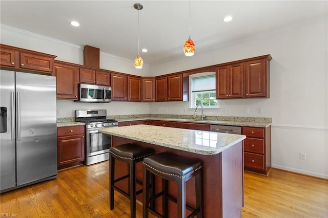 kitchen featuring stainless steel appliances, a sink, light wood-style flooring, a kitchen island, and a kitchen bar