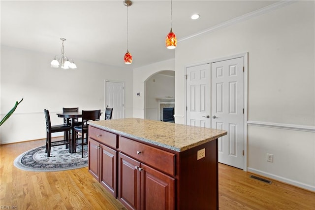 kitchen with arched walkways, a center island, light wood-type flooring, hanging light fixtures, and crown molding