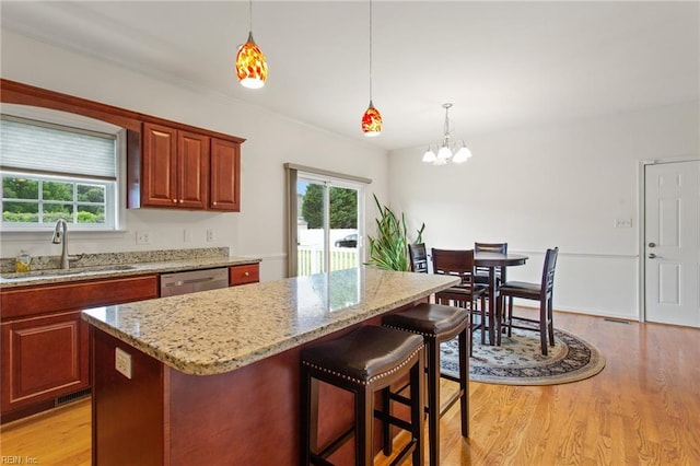 kitchen featuring a sink, a chandelier, light wood-style flooring, stainless steel dishwasher, and light stone counters