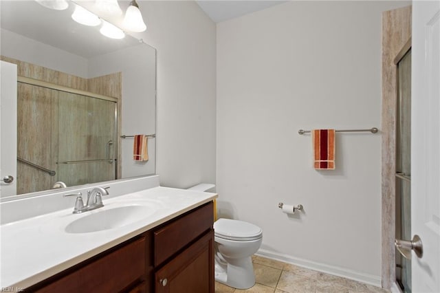 bathroom with a shower stall, toilet, vanity, baseboards, and tile patterned floors