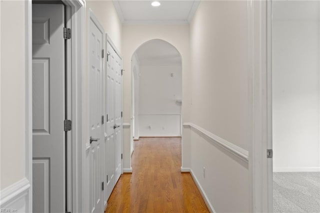 hall featuring arched walkways, ornamental molding, light wood-style floors, and baseboards