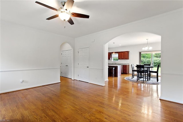 unfurnished living room featuring arched walkways, ceiling fan, light wood finished floors, ornamental molding, and baseboards