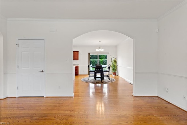 empty room featuring arched walkways, a chandelier, light wood-type flooring, ornamental molding, and baseboards